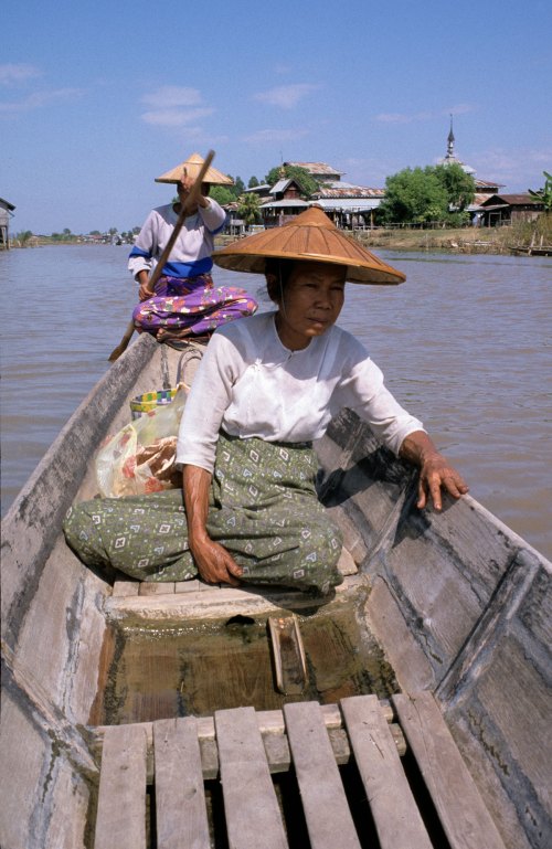 Two Burmese women in sarongs and rice picker's hats row a wooden boat down the canal to Inle Lake, Burma, Myanmar.